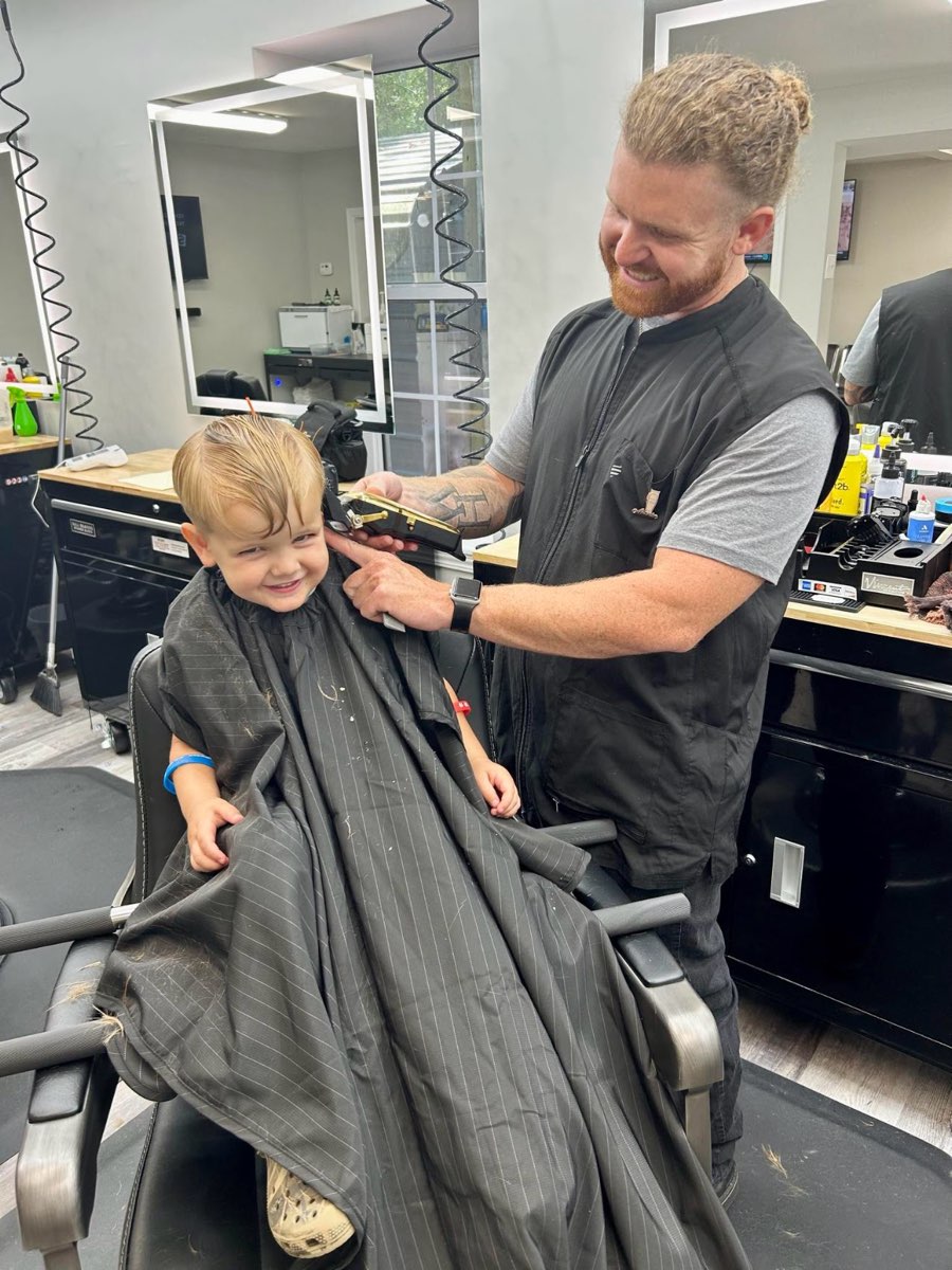 A barber at The People’s Barbershop cutting a smiling young boy’s hair